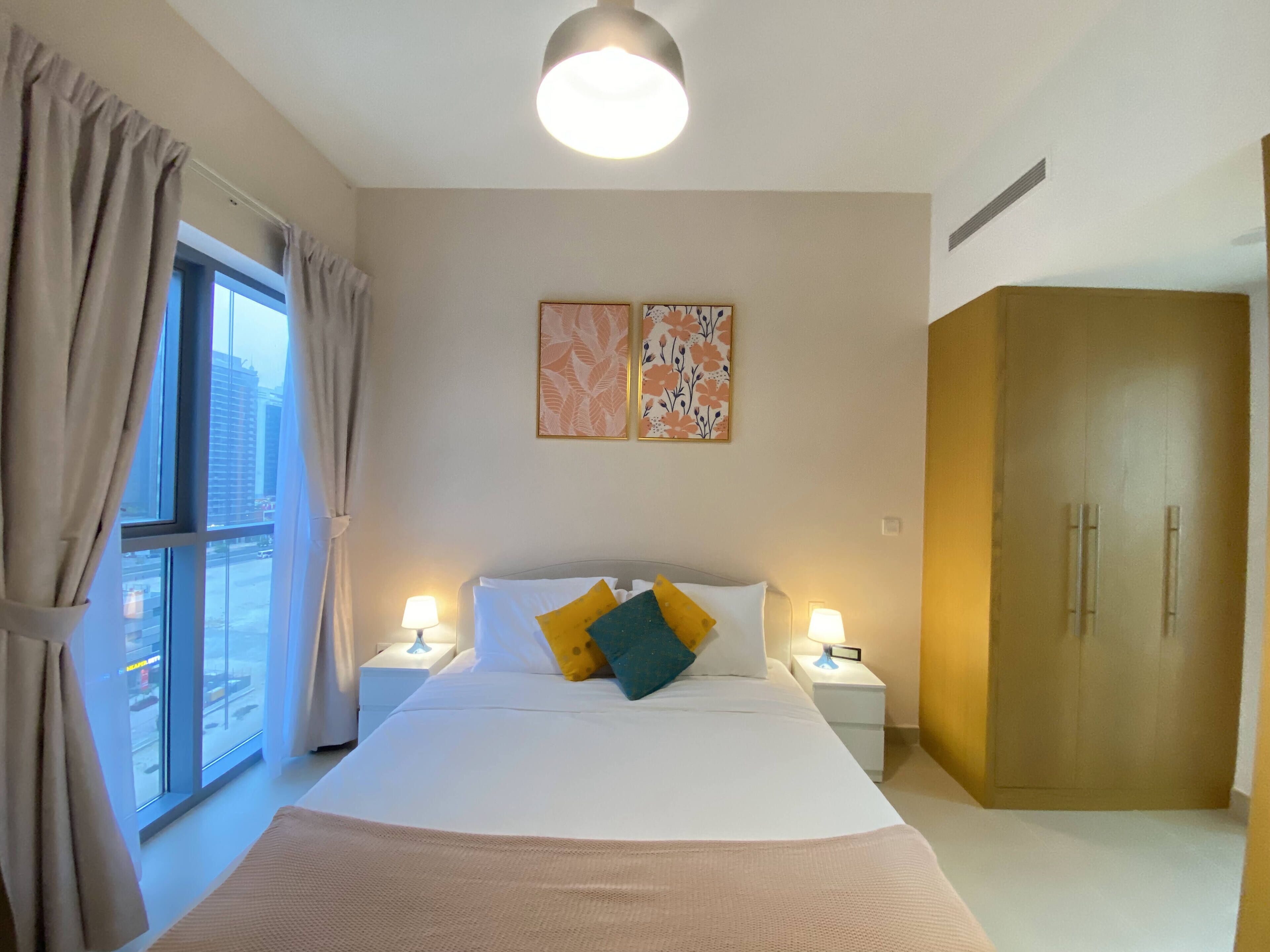 A hotel room with a large bed, two bedside lamps, a window with curtains, and a wardrobe.