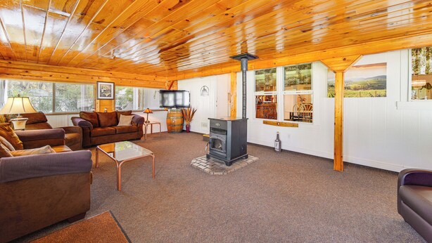 A cozy living room with wooden ceilings, a fireplace, and large windows offering views of the outdoors. - ‘Mtn Gate Guest House’ ~ 6 Mi to Shasta Lake! (Redding)