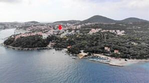 An aerial view of a coastal town with a marina, dense forested hills, and a prominent red arrow pointing to a specific location. - Hotel D-Elegant Dubrovnik (Dubrovnik)