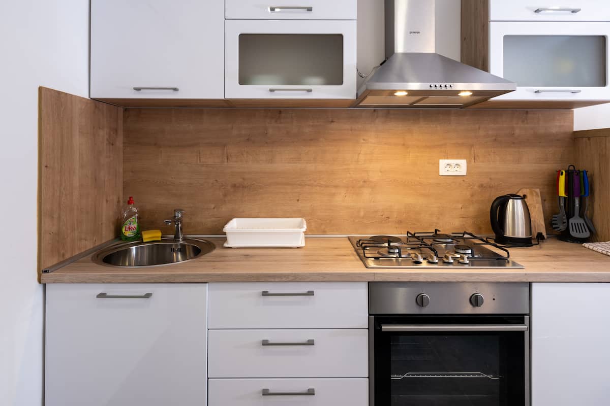Eine moderne Küche mit weißen Schränken, einer Edelstahl-Spüle, einem Gasherd und einem Backofen.