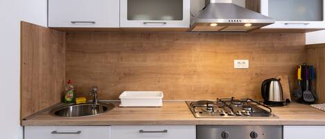 Una cocina moderna con gabinetes blancos, un lavamanos de acero inoxidable, una estufa a gas y un horno.