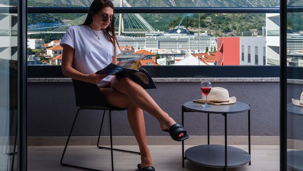 A person sitting on a chair by a window overlooking a bridge and mountains. - Hotel D-Elegant Dubrovnik (Dubrovnik)