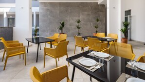 A modern dining area with yellow chairs and black tables, featuring potted plants and a grey tiled wall. - Hotel D-Elegant Dubrovnik (Dubrovnik)