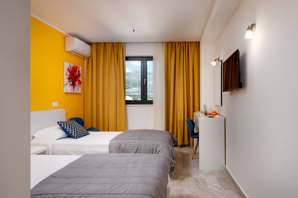 Ein Hotelzimmer mit zwei Betten, einem Schreibtisch, einem Stuhl, einem Fernseher und einem Fenster mit Vorhängen.