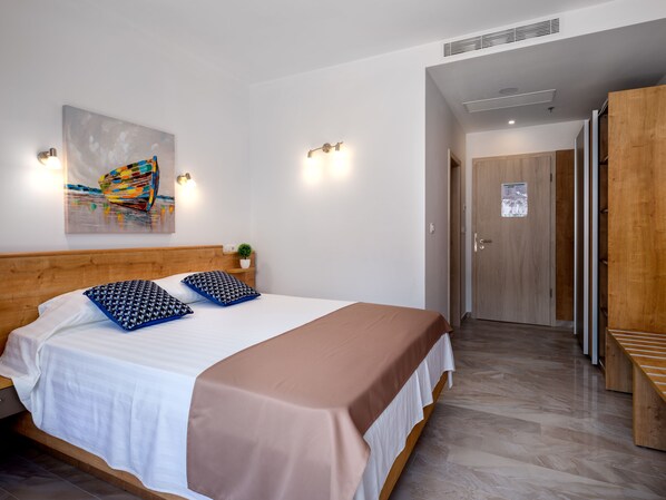 A neatly arranged bedroom with a wooden headboard, a bed with white and brown bedding, a colorful abstract painting, and two wall-mounted lights. - Hotel D-Elegant Dubrovnik (Dubrovnik)