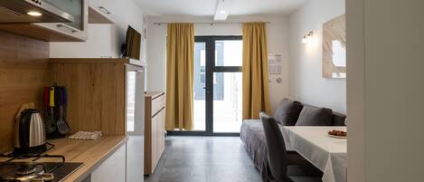 A compact kitchen with modern appliances, a dining area with a table and chairs, and a view through a door.