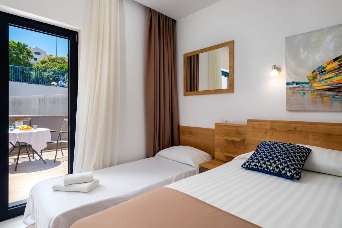Ein Hotelzimmer mit zwei Betten, einem Essbereich mit Tisch und Stühlen, einer Glasschiebetür nach draußen und einem Bild an der Wand.