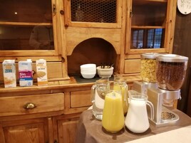 Preparación para el desayuno con diversos productos lácteos, entre ellos leche y leche de almendras, y un exprimidor con jugo fresco.