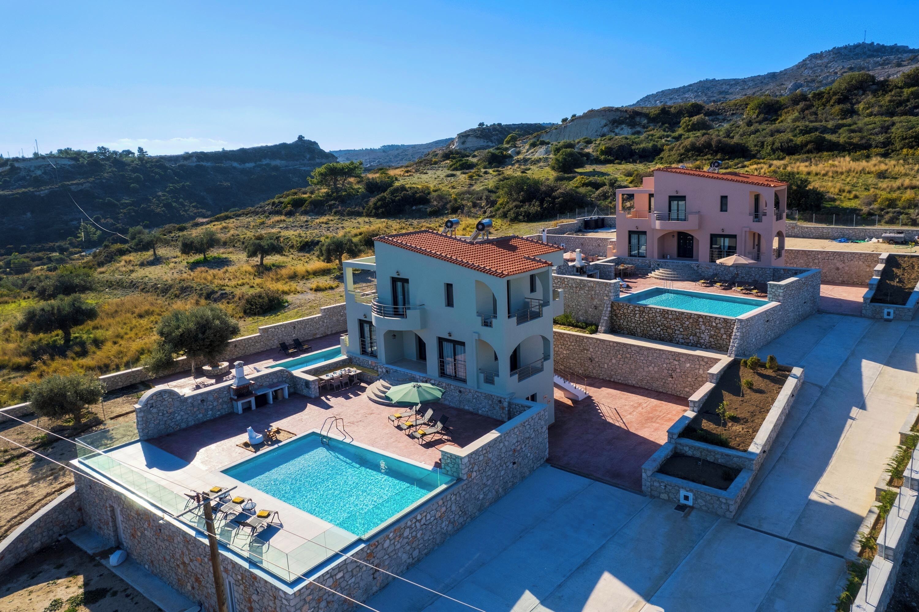 Una villa moderna con piscina, pareti in pietra e vista sulle colline circostanti.