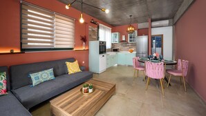 Ein modernes Wohnzimmer mit Sofa, Couchtisch, Esstisch mit Stühlen, Küchenzeile und Deckenbalken.
