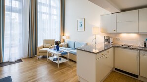 A modern hotel room with a living area, a kitchenette, and a large window with curtains. - Galerieappartement zur Südseite (Juist)