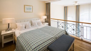A hotel room with a large bed, two bedside tables, a bench, a view of the balcony, and a framed picture on the wall. - Galerieappartement zur Südseite (Juist)