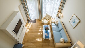 A modern living room with a sofa, armchair, and coffee table. There is a fireplace, a TV, and a window with curtains. - Galerieappartement zur Südseite (Juist)