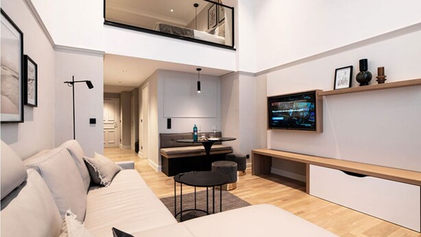 A modern living space with a sofa, a dining table, and a TV mounted on the wall. - Galerieappartement zur Südseite (Juist)
