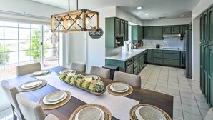 Una cocina moderna con armarios verdes, un comedor con mesa de madera dispuesta para cuatro, y una lámpara colgante.