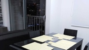 A dining area with a black table and chairs, a window with a view of the city at night, and a balcony with a railing.