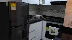 A compact kitchen with white cabinets, a black refrigerator, a tiled backsplash, and a gas stove.