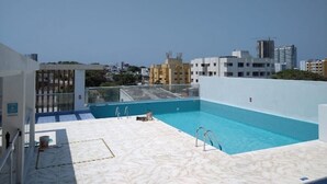 A rooftop pool with clear blue water, surrounded by a white tiled deck.