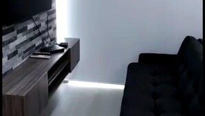 A modern living room with a black sofa, a flat-screen TV mounted on a wall with a patterned design, and a wooden entertainment unit.