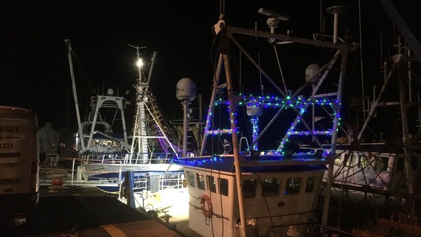 A marina at night with boats docked, illuminated by string lights.