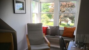A cozy seating area with a cushioned chair, a bench with pillows, and a dining table with cutlery and a glass.