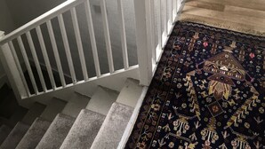 A staircase with a white railing leading to a kitchen area with a coffee maker, a red tray, and a dishwasher.