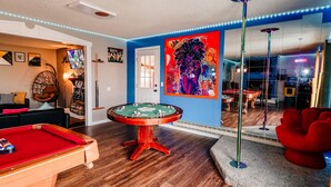 Une pièce avec une table de billard, un canapé rouge, un fauteuil et un grand miroir qui reflète une table de billard.