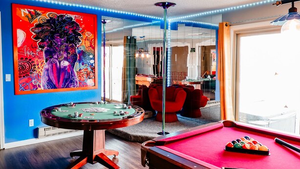 Une pièce équipée d’une table de billard, d’un baby-foot et ornée d’un grand tableau abstrait au mur.