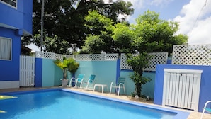 A swimming pool with blue water, surrounded by a white fence, and several lounge chairs. - Queen room at Bellissimo (Scarborugh)