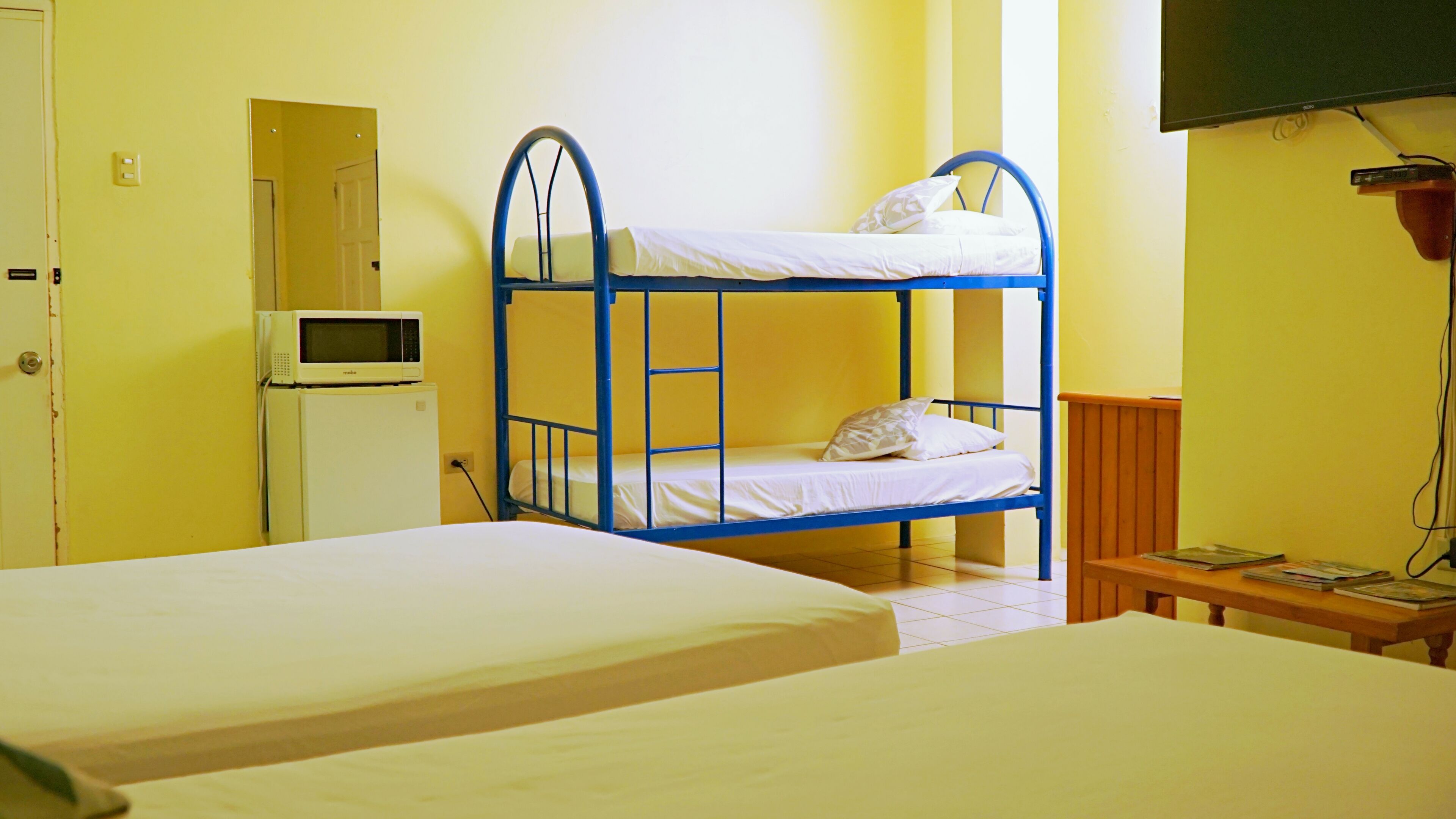 A room with two bunk beds, a small table with books, a microwave, and a television.