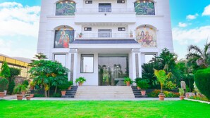 A two-story building with a central entrance, surrounded by a well-maintained garden with various plants and a clear sky. - The Pure Nature Hotel (Rajgarh)