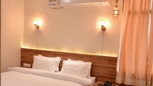 A hotel room with a wooden bed, a nightstand, a ceiling fan, an air conditioning unit, and two wall-mounted lamps. - The Pure Nature Hotel (Rajgarh)