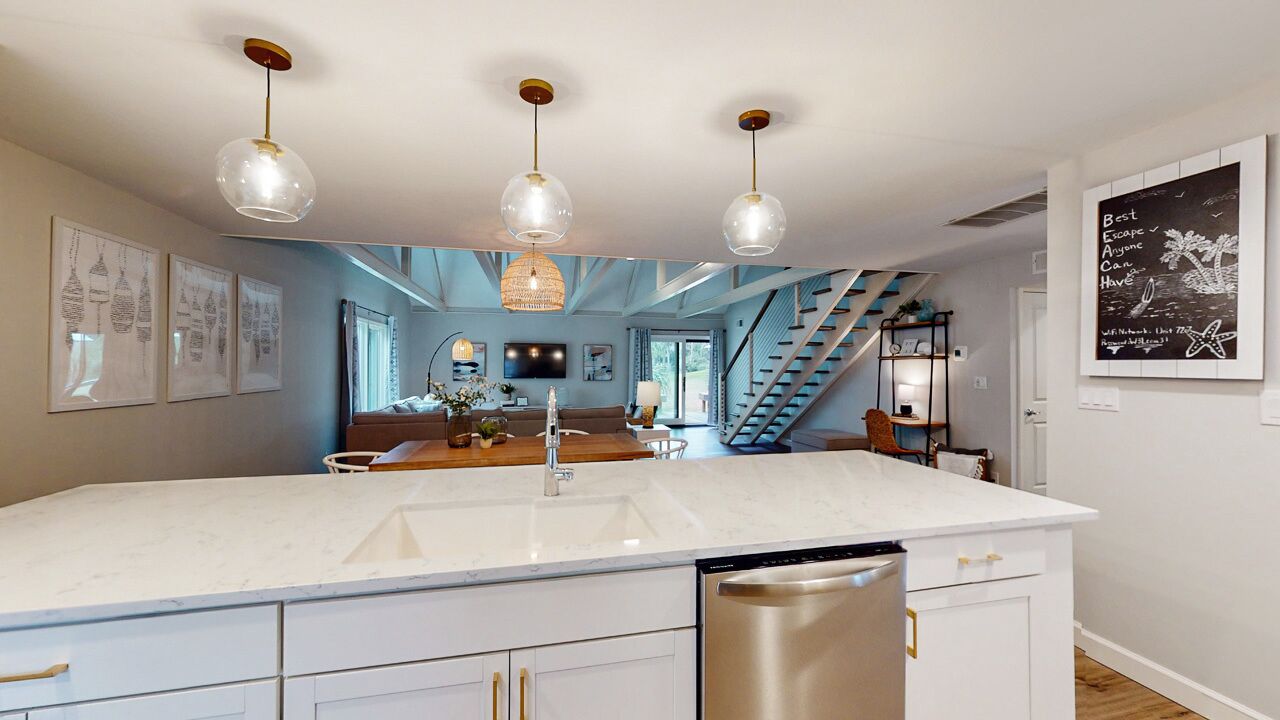Una cocina moderna con una isla grande, luces colgantes y una escalera que sube a otro nivel.