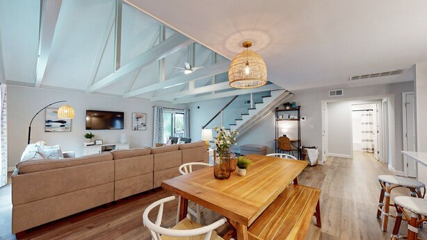 A spacious living area with a wooden dining table, a sofa, and a staircase leading to an upper level.