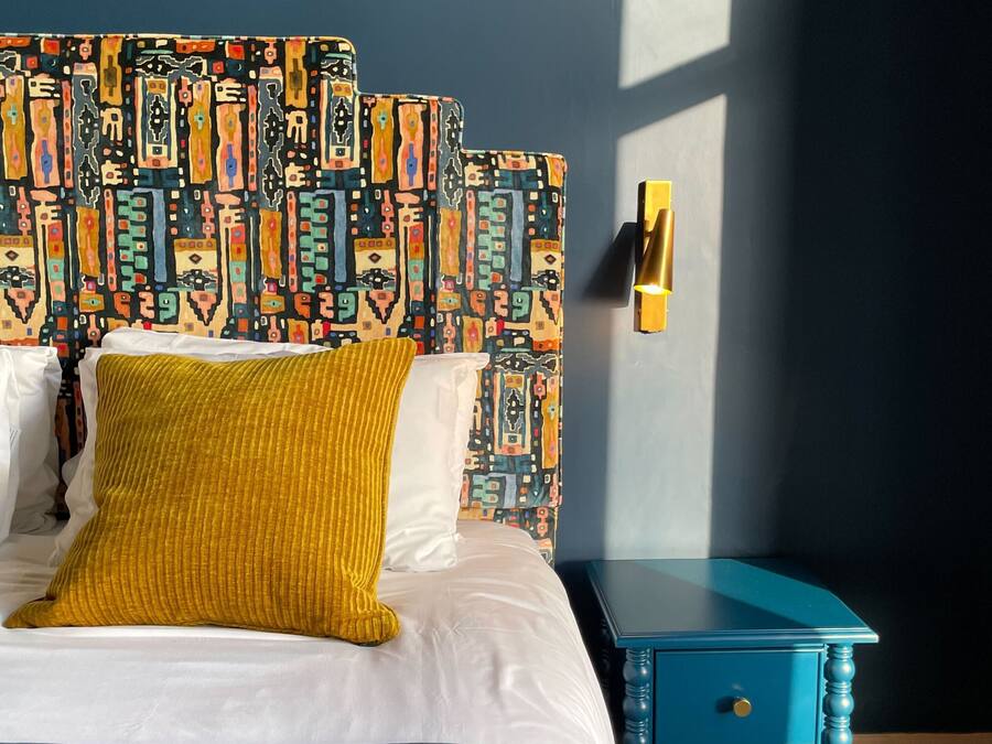 A bed with a patterned headboard, a mustard-colored throw, and a blue nightstand with drawers.