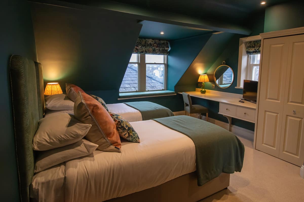 A bedroom with two beds, a desk, a chair, a wardrobe, and a window with a view.