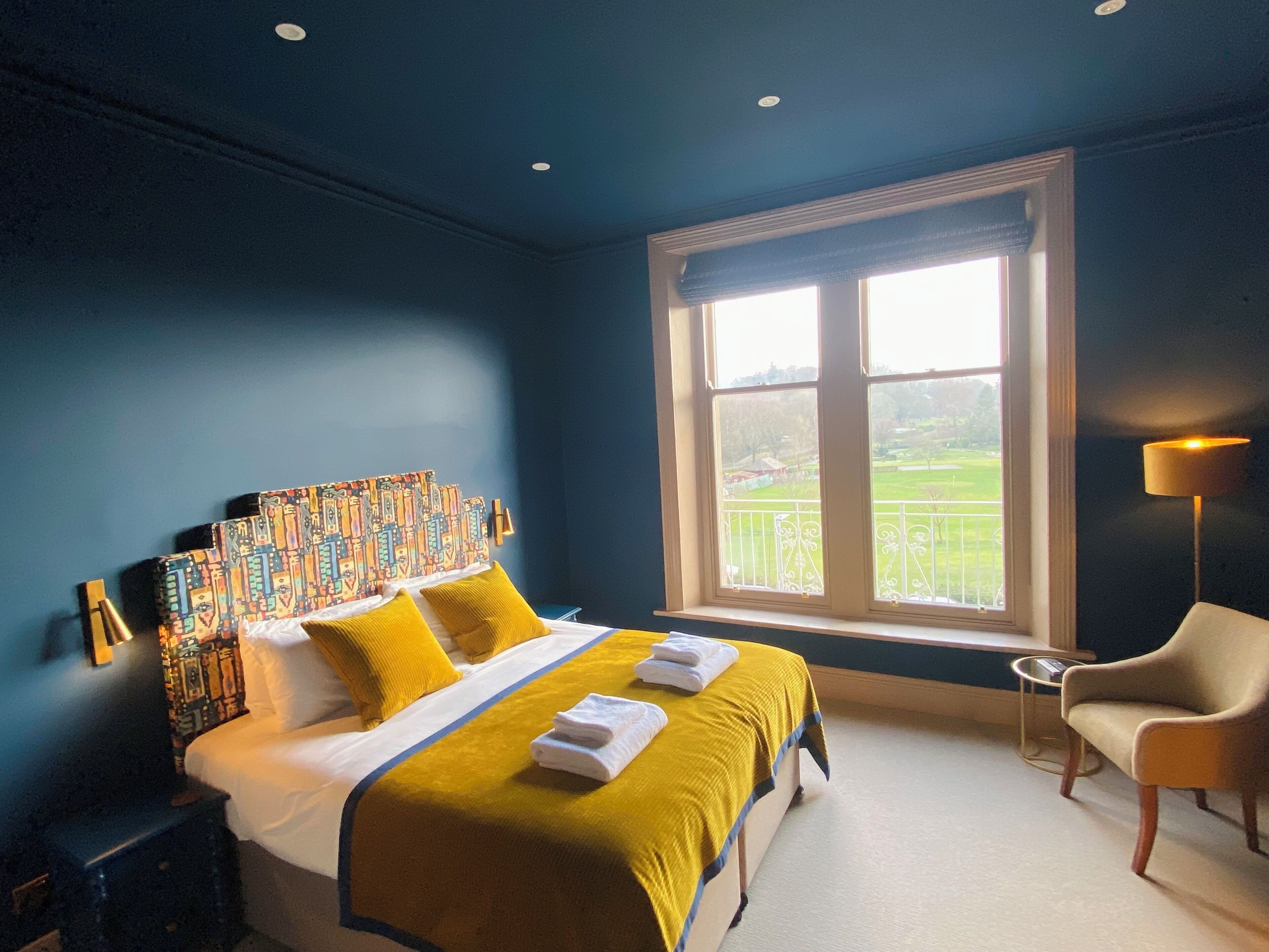 A bedroom with a large bed, a window with a view, a chair, and a lamp.