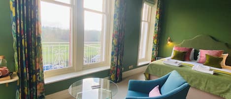 A room with a bed, two chairs, a glass table, and large windows with curtains.