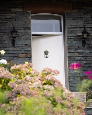 A white door with a decorative handle, set in a stone wall with two black lantern-style lights.