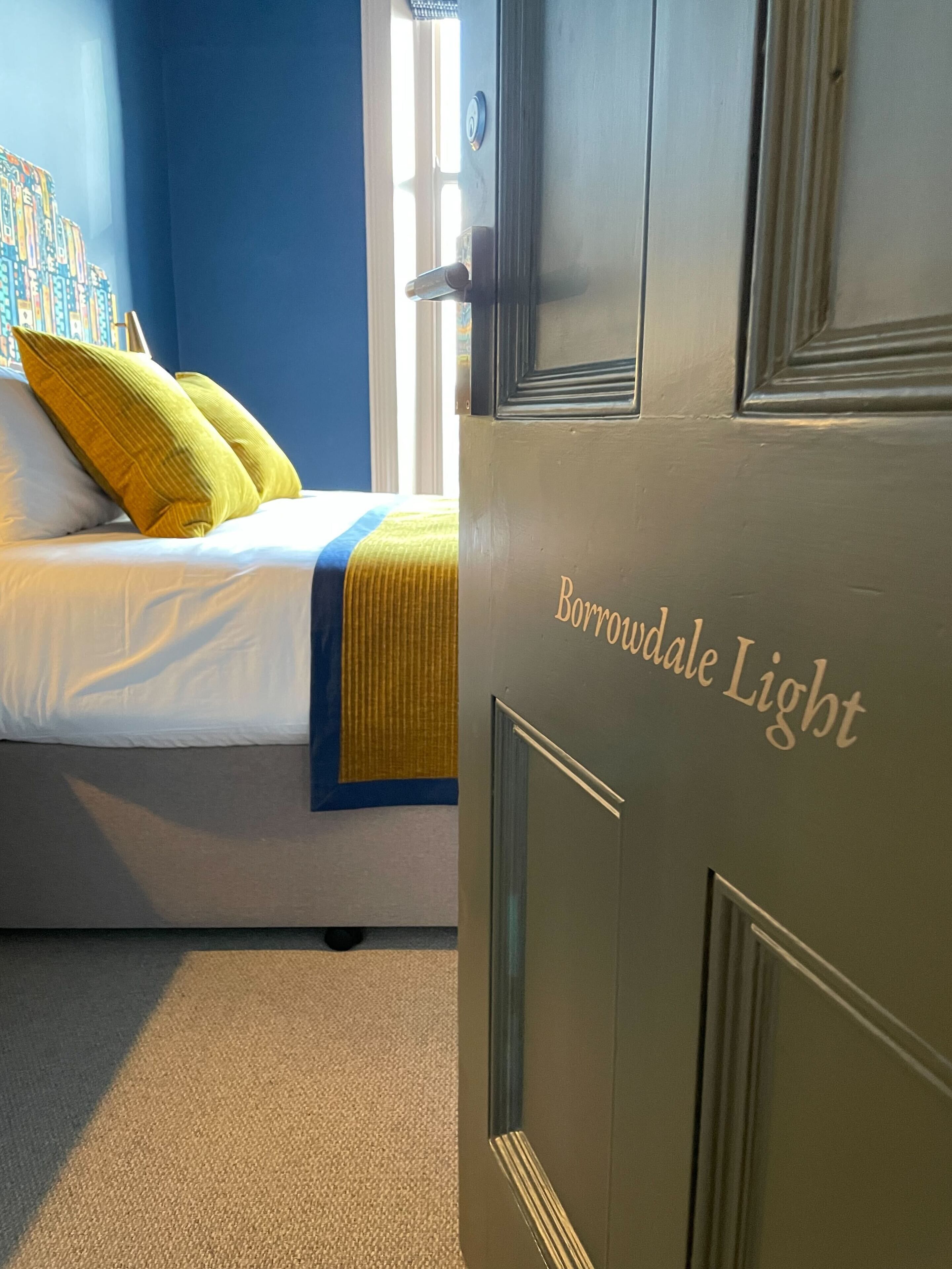 A bedroom with a bed, pillows, and a door labeled "Borrowdale Light".