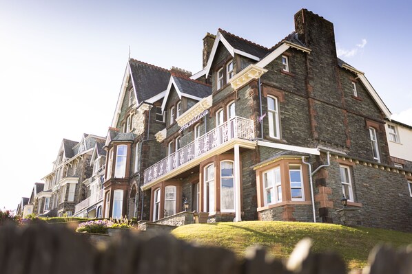 A large, historic stone building with multiple stories, large windows, and a prominent balcony.
