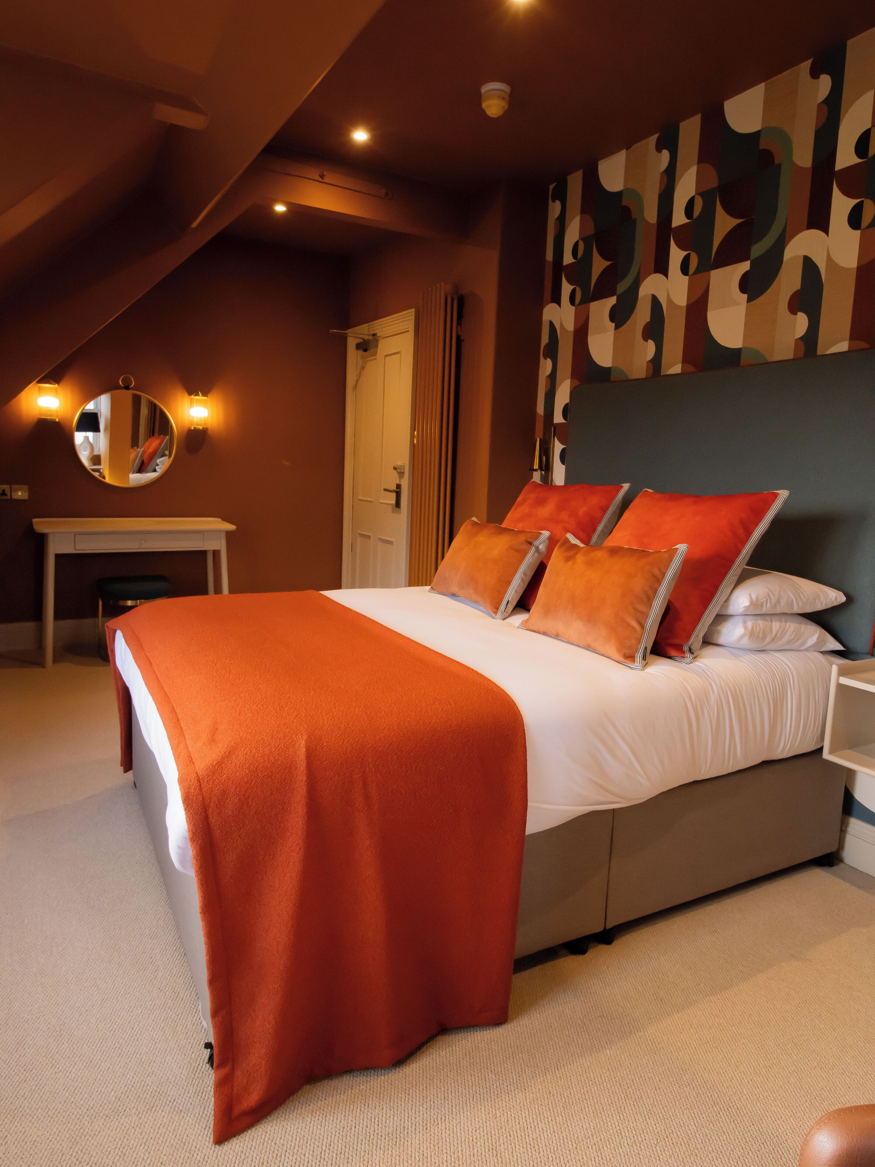 Ein Schlafzimmer mit einem Bett, einem Nachttisch, einem Spiegel und einer Wand mit abstrakter Kunst.