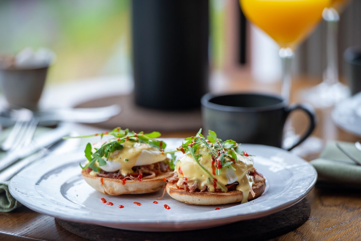 Une assiette de petit-déjeuner avec des œufs Bénédicte et un verre de jus d’orange.
