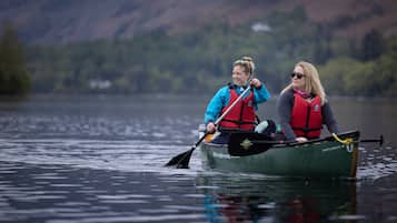 Two people in a green canoe on a calm lake with mountains in the background.