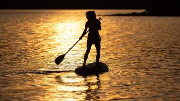 A silhouette of a person paddleboarding on calm water during sunset.