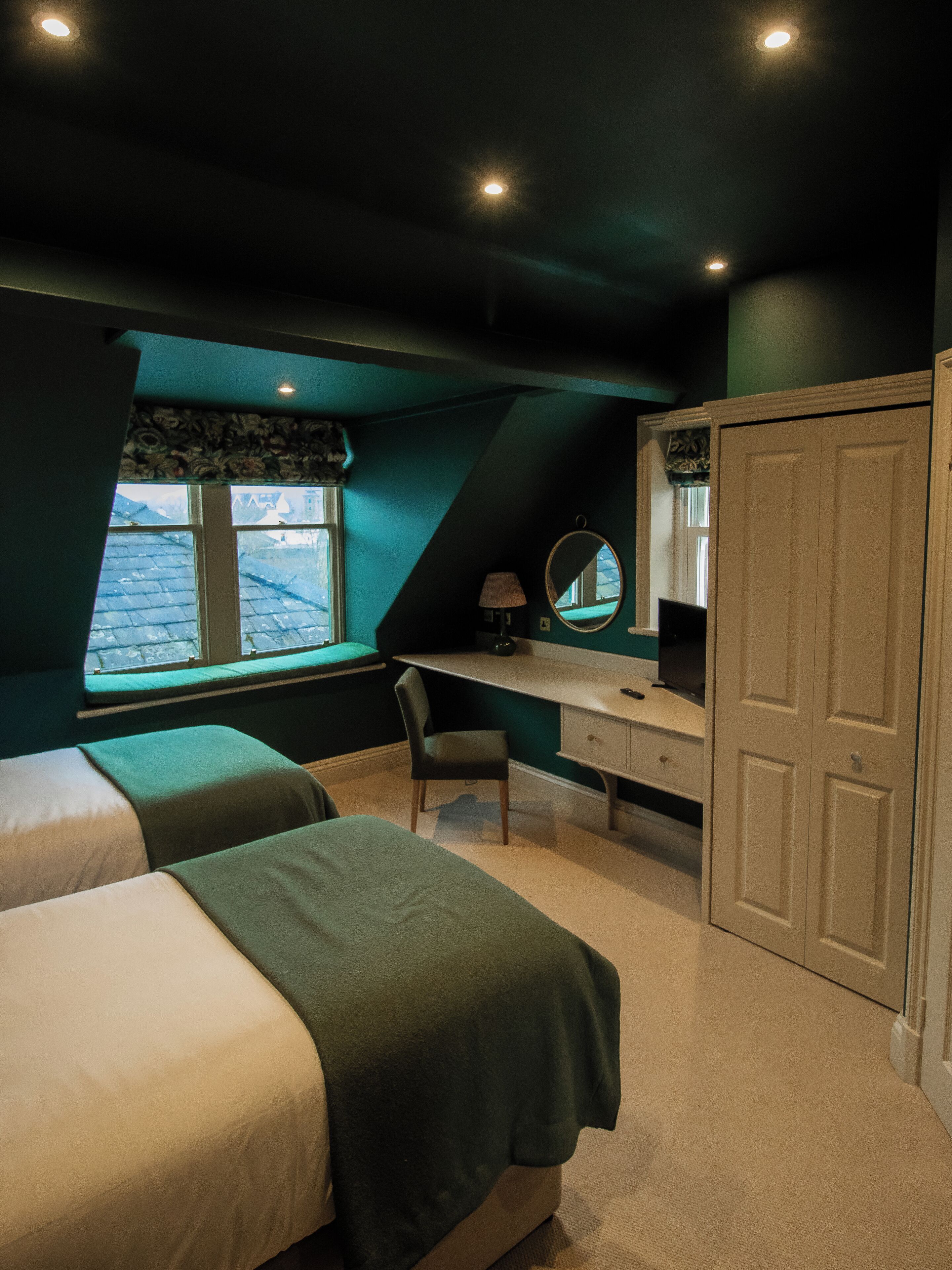Un dormitorio con dos camas, un escritorio, una silla, un armario y una ventana con vistas al exterior.