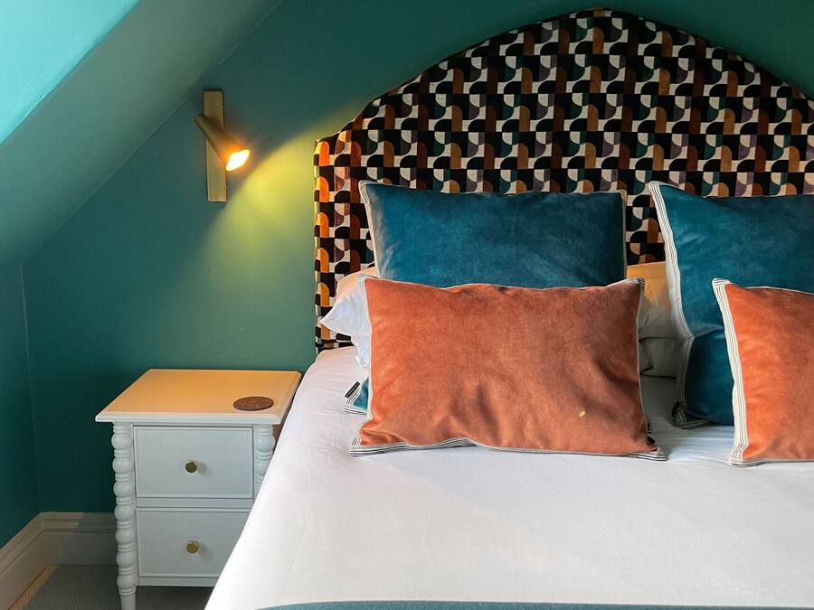 A bedroom with a patterned headboard, a bedside table, and a bed with multiple pillows.