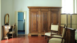 Une pièce comprenant une armoire en bois, une chaise, un bureau avec un miroir et une porte donnant sur une autre pièce.