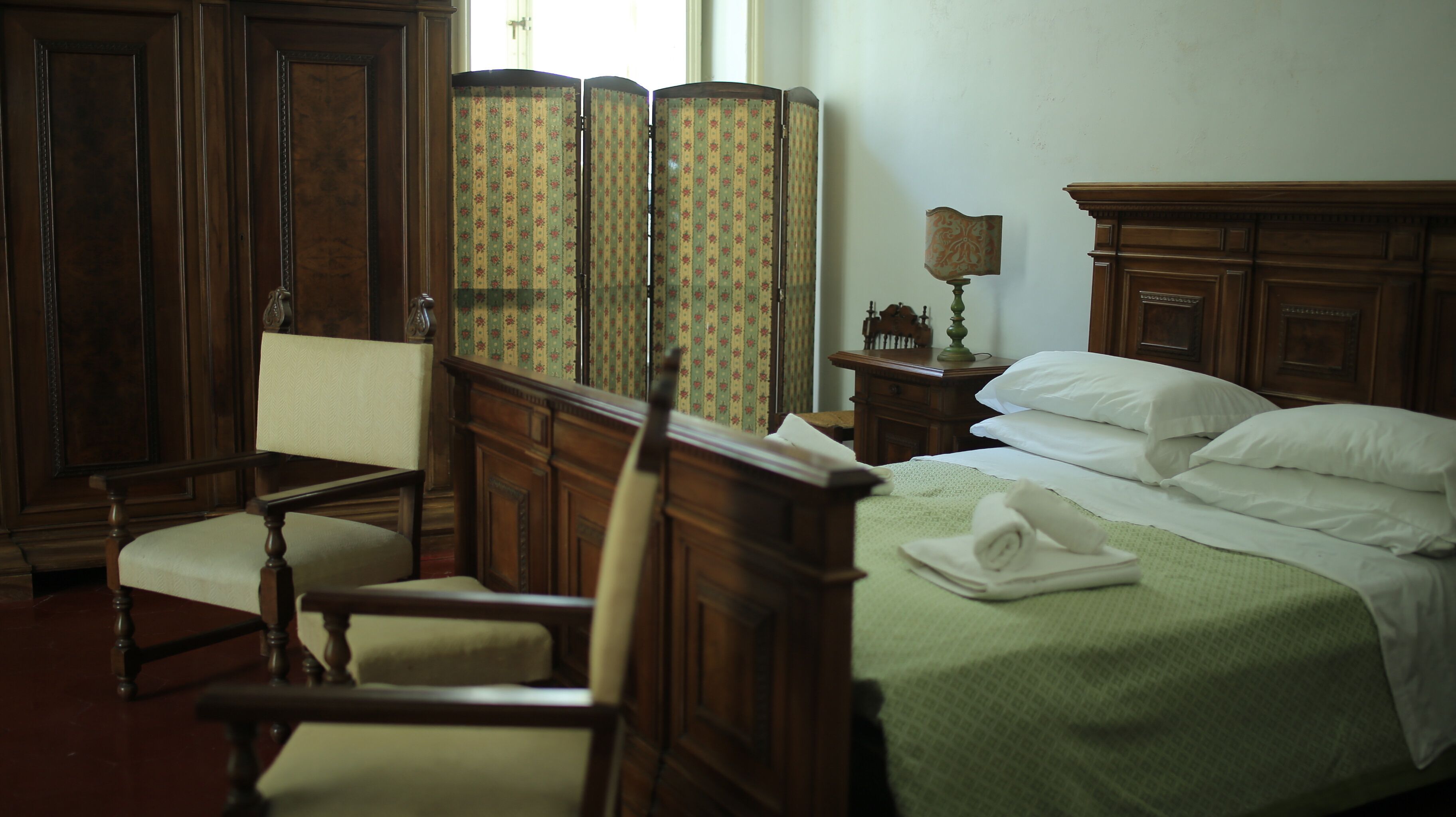 A traditional room with a wooden bed, a chair, a nightstand, and a wardrobe.