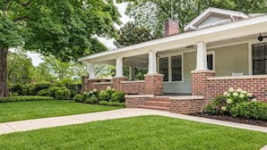 A two-story house with a covered porch, brick exterior, and a well-maintained lawn. - Adorable Home. Close to Everything. Great Location (Charlotte)